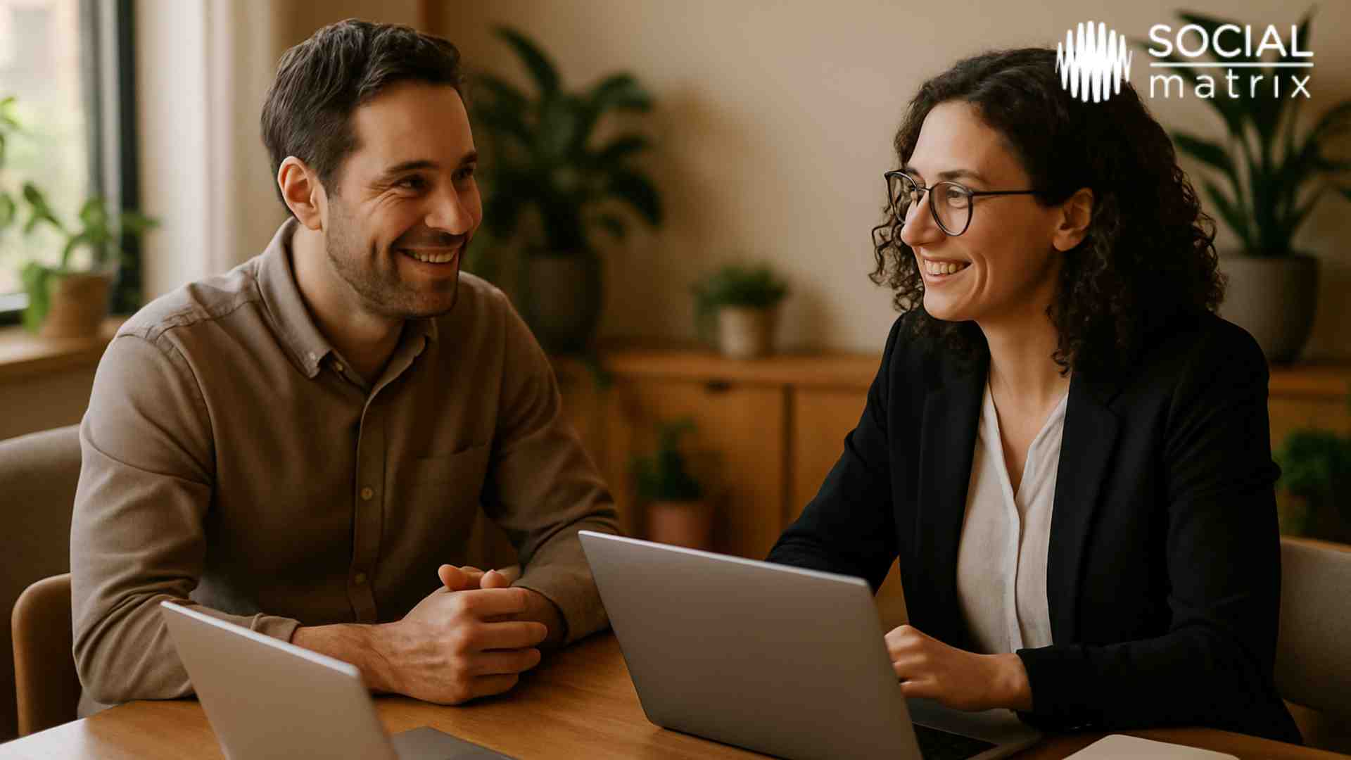 Professional consultation meeting between small business owner and digital marketing partner discussing strategy with laptops on wooden table