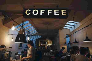 Interior of a busy café with a large illuminated sign reading 'COFFEE' hanging from the ceiling.
