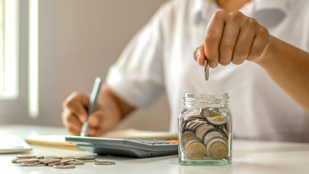 Problems with digital marketing agencies often show up in rising costs — image of a person adding coins to a jar while calculating expenses.