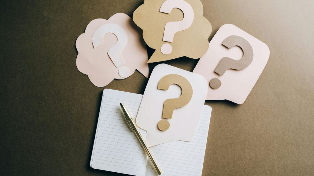 Confusion is one of the common problems with digital marketing agencies — paper question marks on a desk beside a notebook and pen.
