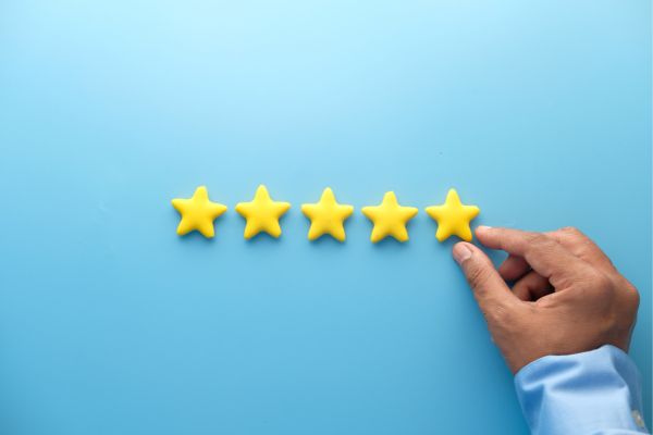 A person’s hand placing the last of five yellow stars on a blue background, representing customer reviews.