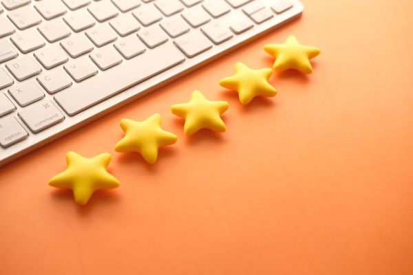 A white computer keyboard with five yellow stars arranged in a row on an orange background, representing customer reviews.