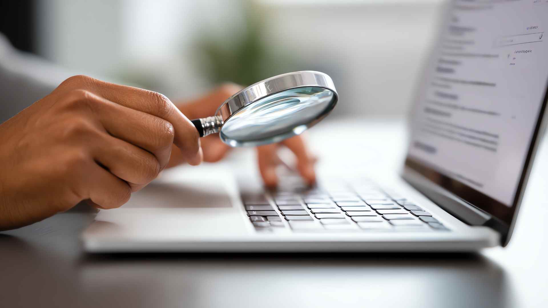 A close-up of a person holding a magnifying glass over a laptop keyboard while searching online. The image represents checking business information and verifying local SEO citations.