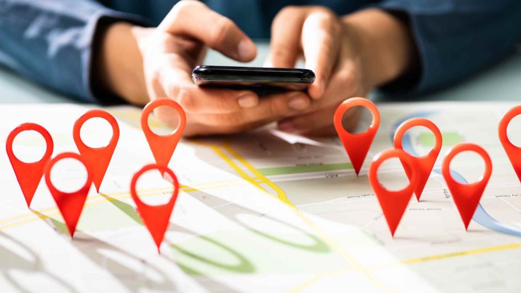 A person using a smartphone above a map covered with red location markers. The image highlights how local SEO citations support accurate location data for businesses.