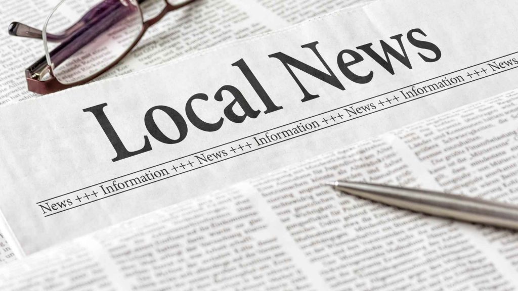 A newspaper with the headline “Local News,” placed beside reading glasses and a pen. The image reflects how community sources and mentions contribute to unstructured local SEO citations.